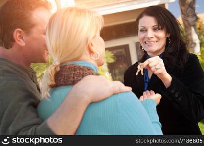 Hispanic Female Real Estate Agent Handing Over New House Keys to Happy Couple In Front of House.