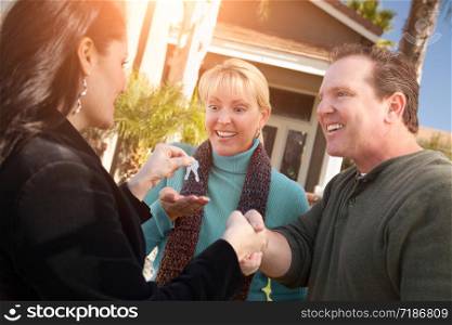 Hispanic Female Real Estate Agent Handing Over New House Keys to Happy Couple In Front of House.