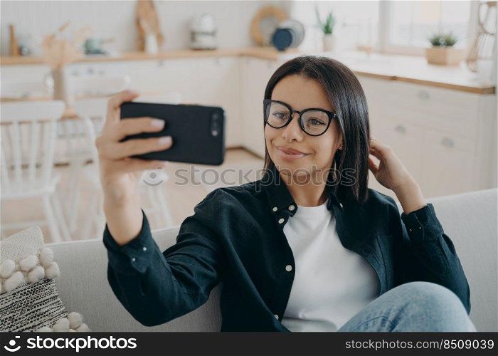 Hispanic girl is making selfie on smartphone. Woman is relaxing and using mobile phone camera. European lady enjoying time at home. Mobile phone, technologies and application using.. Hispanic girl is making selfie on smartphone. Woman is relaxing and using mobile phone camera.