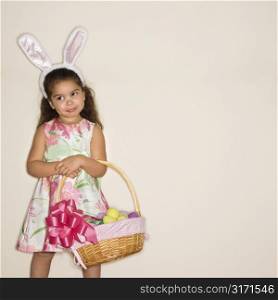 Hispanic girl wearing bunny ears holding Easter basket.