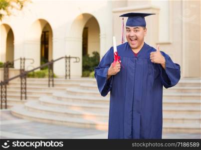 Hispanic Male With Deploma Wearing Graduation Cap and Gown On Campus.