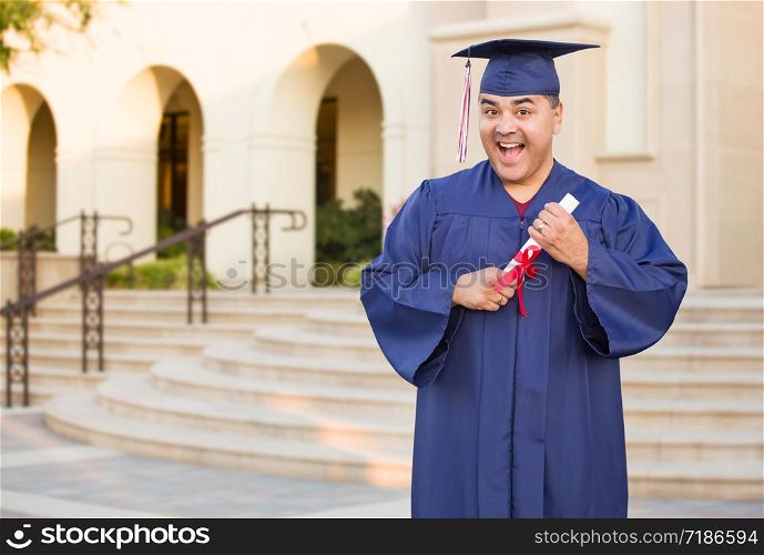 Hispanic Male With Deploma Wearing Graduation Cap and Gown On Campus.