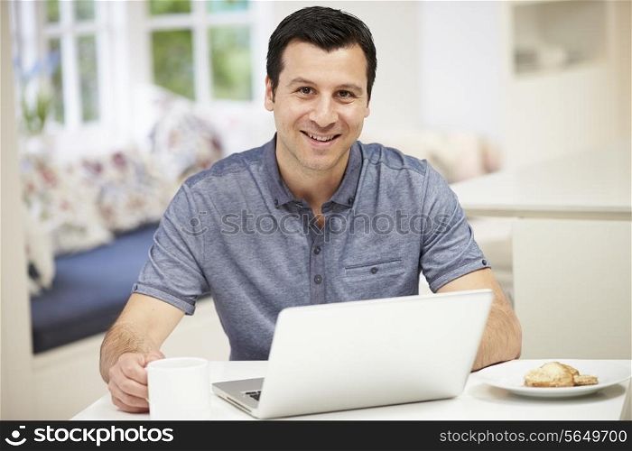 Hispanic Man Using Laptop In Kitchen At Home