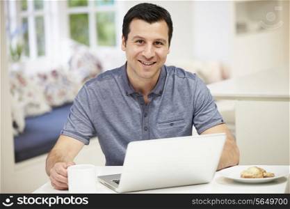 Hispanic Man Using Laptop In Kitchen At Home