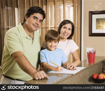 Hispanic parents and son with homework smiling at viewer.