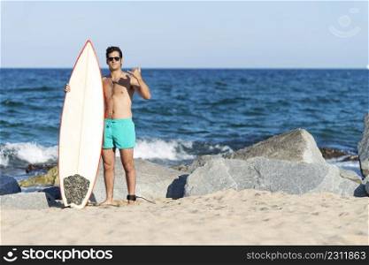 Hispanic surfer man with sunglasses holding a surfer board at sea shore