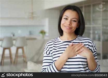 Hispanic woman keeps hands close to heart. Conceptual portrait of young happy woman showing love. Positive trendy girl in sailor shirt at home. Advertising banner mockup with copyspace.. Hispanic trendy girl in sailor shirt keeps hands close to heart. Happy woman showing love.