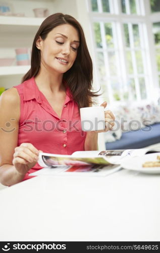 Hispanic Woman Reading Magazine In Kitchen At Home