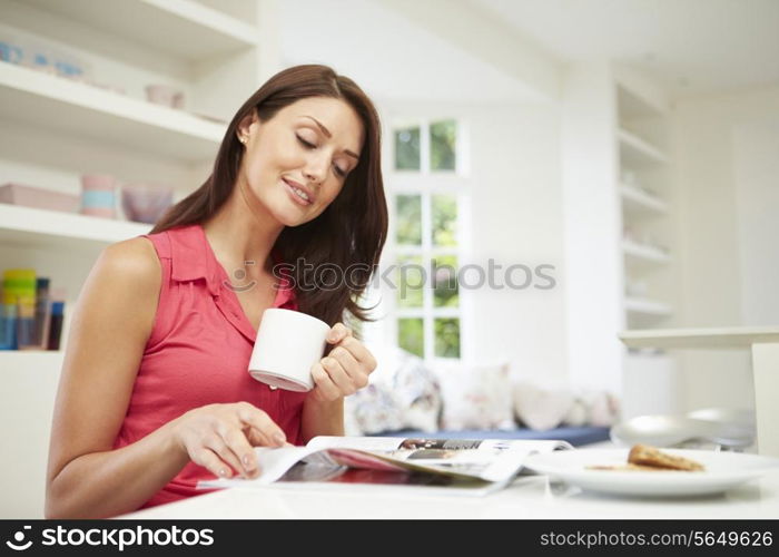 Hispanic Woman Reading Magazine In Kitchen At Home