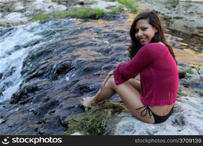 Hispanic woman sitting at water edge of a creek.
