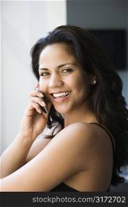 Hispanic young adult woman looking at viewer and talking on cell phone.