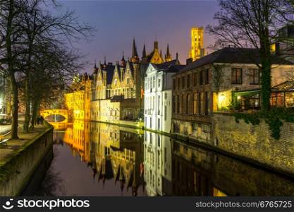 Historic medieval buildings along a canal in Bruges, Belgium at dusk.