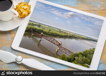 Historic railroad Katy Bridge over Missouri River at Boonville - reviewing aerial image on a digital tablet with a cup of coffee