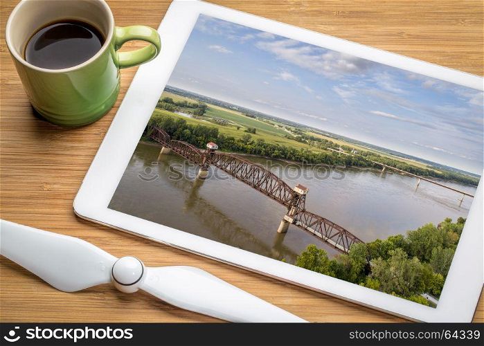 Historic railroad Katy Bridge over Missouri River at Boonville - reviewing aerial image on a digital tablet with a cup of coffee
