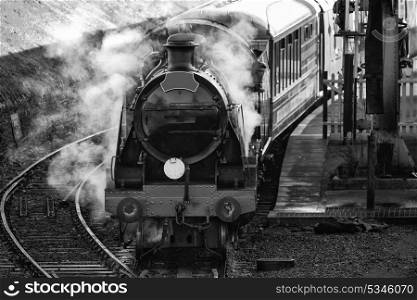 Historic vintage steam railway engine in station with full steam puffing in black and white