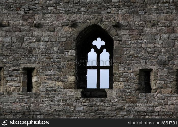 Historic wall of gray stones with window and cross as a window rung