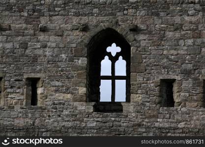 Historic wall of gray stones with window and cross as a window rung