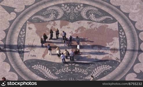 Historischer Platz aus Stein-Mosaik in Lissabon; Es stellt die Weltkarte dar und die wichtigsten Entdeckerreisen sind eingezeichnet. Menschen sind auf dem Platz.