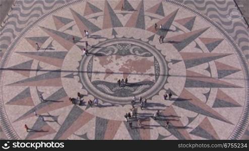 Historischer Platz aus Stein-Mosaik in Lissabon; Es stellt die Weltkarte dar und die wichtigsten Entdeckerreisen sind eingezeichnet. Menschen sind auf dem Platz.