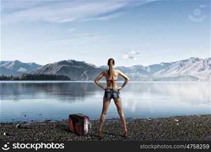Hitch hiker woman on riverside. Beautiful woman in swimsuit standing with back and enjoying picturesque view