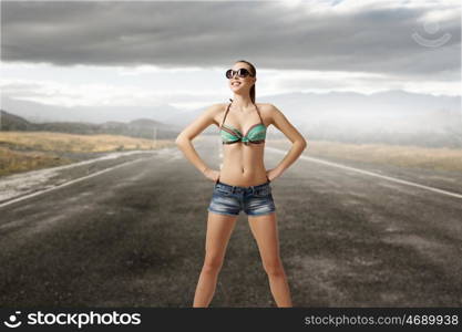 Hitch hiker woman on road. Young attractive girl in bikini and shorts on road