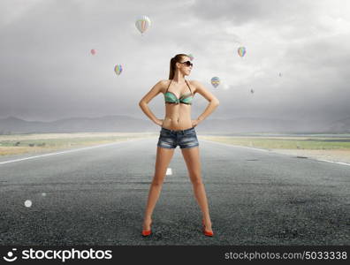 Hitch hiker woman on road. Young attractive girl in bikini and shorts on road