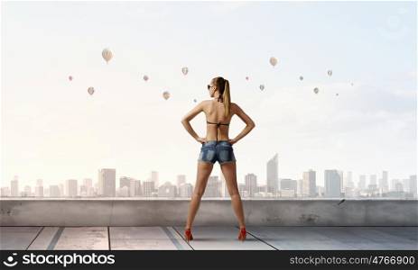 Hitch hiker woman on roof. Young attractive girl in bikini and shorts on building roof