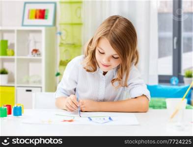 hobby, art and childhood concept - happy smiling girl with brush and colors drawing picture over home room background. happy girl with brush and colors drawing at home