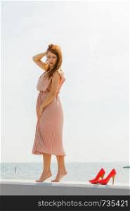 Hobby, idyllic aspects of femininity concept. Woman walking on jetty without shoes wearing beautiful long light pink dress.. Woman wearing long light pink dress on jetty
