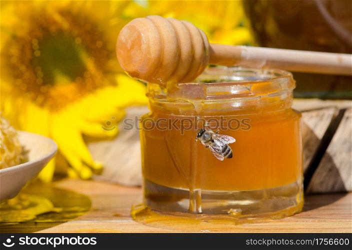 Hohey in glass jars and western honey bee. Honey Bee on nature background . Bee sitting on glass of honey. Honey in glass jar with flying honey bee
