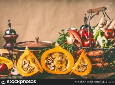 Hokkaido Pumpkins on kitchen table with cooking pot and ingredients at rustic wall background, front view. Healthy vegetarian food and eating concept. Autumn seasonal eating