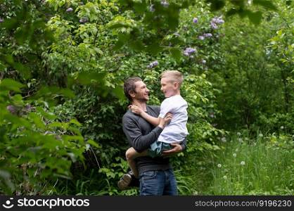 holding a child in your arms, sitting in your arms, studying, dad, son, child, father, parenting, interest development, watching, playing, family vacation, nature walk, spring, flowering tree. The boy is sitting in Dad’s arms and they are laughing