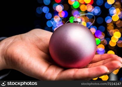 Holding Christmas decoration against bokeh lights background