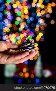 Holding Christmas pine cone decoration isolated on background with blurred lights. December season, Christmas composition.