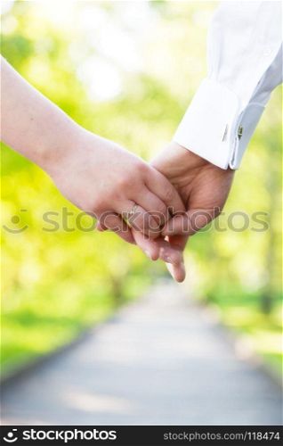 Holding hands close-up. Couple in love dating in summer park. Woman in dress and man wearing elegant shirt. View from the back. Date, fiance with fiancee, hand in hand concepts. Holding hands close-up. Couple in love dating