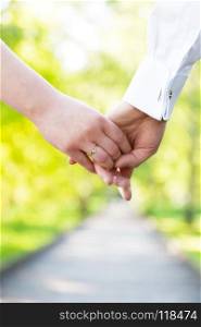 Holding hands close-up. Couple in love dating in summer park. Woman in dress and man wearing elegant shirt. View from the back. Date, fiance with fiancee, hand in hand concepts. Holding hands close-up. Couple in love dating