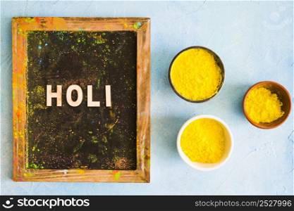 holi text messy wooden slate with yellow holi colored bowls painted backdrop