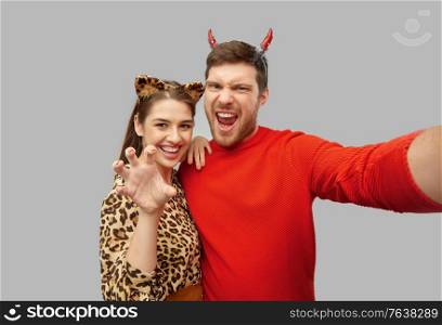 holiday and people concept - happy couple in halloween costumes of devil and leopard taking selfie over grey background. happy couple in halloween costumes taking selfie
