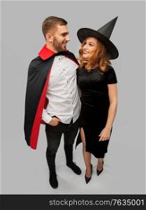 holiday and people concept - happy smiling couple in halloween costumes of vampire and witch over grey background. couple in halloween costumes of witch and vampire