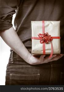 Holiday and special occasion. Closeup of male hands. Man giving golden gift box with red ribbon isolated on white. Guy hiding present behind his back. Surprise. Studio shot.