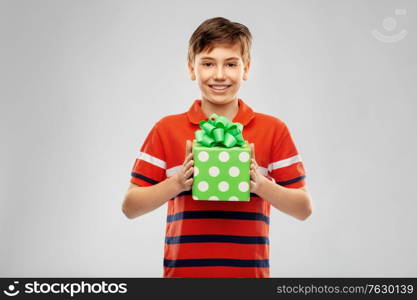 holiday, birthday present and people concept - portrait of happy smiling boy in red polo t-shirt with gift box over grey background. portrait of happy smiling boy with gift box