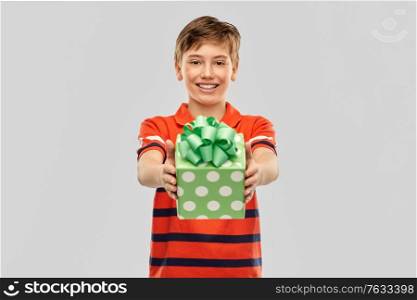 holiday, birthday present and people concept - portrait of happy smiling boy in red polo t-shirt with gift box over grey background. portrait of happy smiling boy with gift box