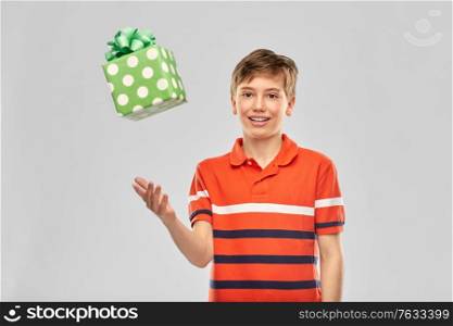 holiday, birthday present and people concept - portrait of happy smiling boy in red polo t-shirt with gift box over grey background. portrait of happy smiling boy with gift box