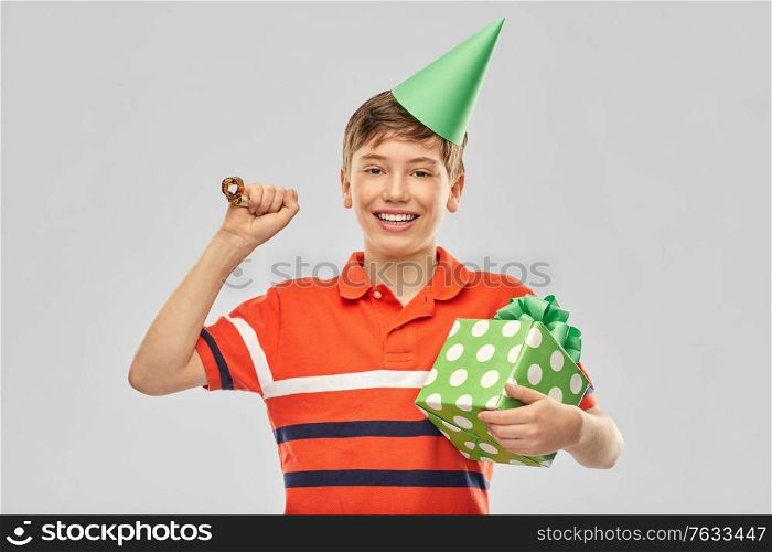 holiday, birthday present and people concept - portrait of happy smiling boy in party hat with gift box and blower over grey background. happy boy in party hat with birthday gift box