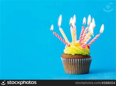 holiday, celebration, greeting and party concept - birthday cupcake with many burning candles over blue background