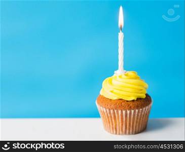 holiday, celebration, greeting and party concept - birthday cupcake with one burning candle over blue background