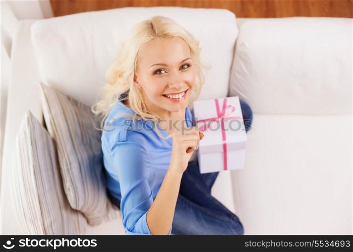 holiday, celebration, home and birthday concept - smiling young woman with gift box and making shh gesture at home