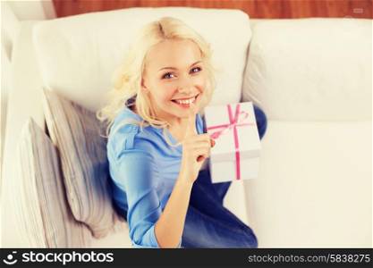 holiday, celebration, home and birthday concept - smiling young woman with gift box and making shh gesture at home