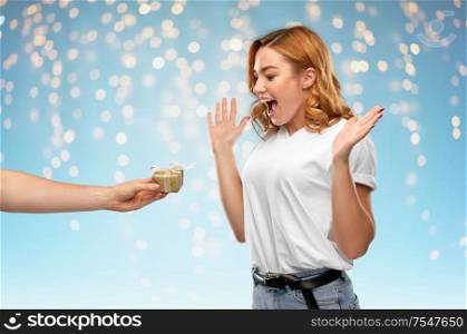 holiday, christmas and valentine&rsquo;s day concept -happy woman in white t-shirt receiving little gift box from man over holidays lights on blue background. happy couple in white t-shirts with christmas gift