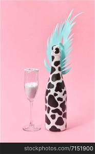 Holiday decorative composition of painted champagne bottle with black spots and paper cut tropical leaf with glass of white powder on a pastel millennial pink background, copy space. Holiday card.. Creative set of painted wine bottle and glass of white powder.